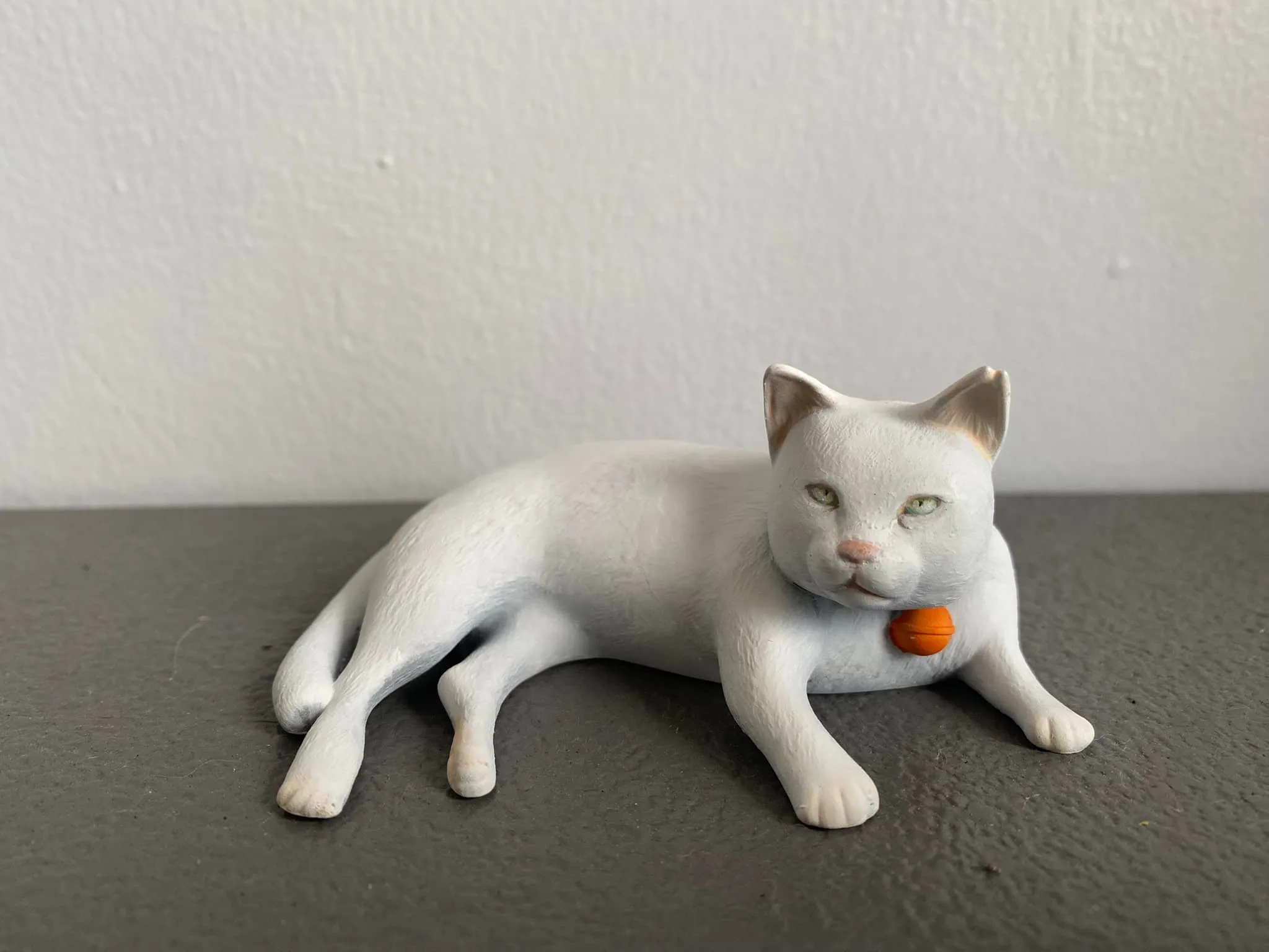 White cat sculpture with a red collar and bell, by Luminary Studios